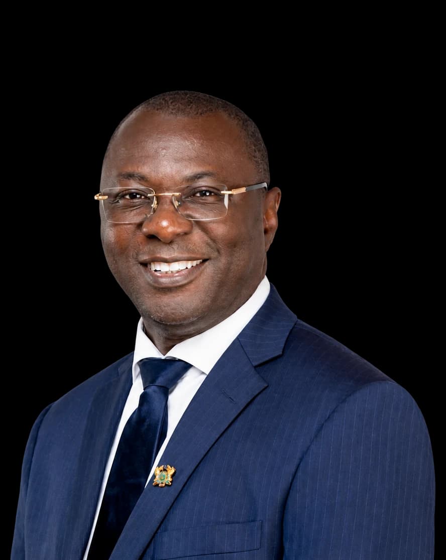 Dr. Mohammed Amin Adam, smiling, wearing glasses and a navy suit with a white shirt and dark tie.
